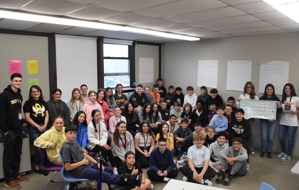 students sitting on floor with one holding large check
